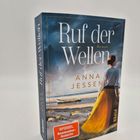 "Ruf der Wellen. Roman. Anna Jessen. SPIEGEL Bestseller-Autorin." Frau am Strand mit Boot im Hintergrund, gelbes Kleid.