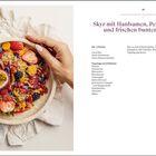 Titel: Skyr mit Hanfsamen, Pekannussbutter und Toppings. Links bunte Schüssel mit Früchten und Granola, Hand hält Schüssel.