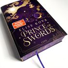 „Spiegel Bestseller-Autorin“, „Elise Kova“, „Prince of Swords“. Das Cover ist lila mit goldenen, himmlischen Verzierungen.