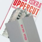 Buch mit rotem Schriftzug „MIJA ISKRA UPPERCUT“ auf dem Rücken. Darunter teilweise sichtbare Hochhäuser.