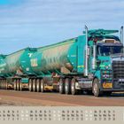 "LKW mit Aufschrift 'TOLL', zieht mehrere Anhänger. Unten Kalender für April 2021. Wüste im Hintergrund."