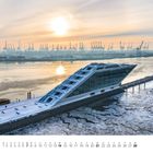 Februar-Kalender mit Zahlen darunter. Schneebedecktes, modernes Gebäude am Wasser, Hafen und Kräne im Hintergrund bei Sonnenaufgang.