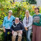 Vier Menschen stehen in einem grünen Garten, ein Mann sitzt im Rollstuhl.