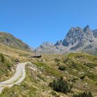 Eine Fahrradfahrerin auf einem Bergweg mit grünen Wiesen und hohen, felsigen Gipfeln. Ein Wegweiser steht auf einem Hügel.