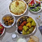 Eine reich gedeckte Tafel mit Reis, gefüllten Paprikaschoten, Salat, Brot und Joghurt auf einem gemusterten Tischtuch.