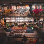Eine gemütliche Bibliothek mit vielen Regalen, Sesseln und Pflanzen, vollständig mit Büchern und gemütlichen Sitzbereichen ausgestattet.