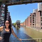 Texte: "NUR DER", "TV", "1". Frau auf Brücke, Wasserkanal, rote Backsteingebäude, sonniger Tag, Sticker auf Metall.