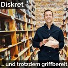 „Diskret … und trotzdem griffbereit“. Ein lächelnder Mann steht zwischen Bücherregalen und hält ein aufgeschlagenes Buch.
