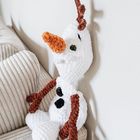 Plüschschneemann mit orangener Nase und braunen Armen sitzt auf einem beige-grauen Sofa an der Wand.