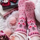 Es sind keine Texte sichtbar. Zwei Rosa-Socken mit geometrischem Muster, rote Herzkerzen in Glasbehältern, Bücher, Pralinen.
