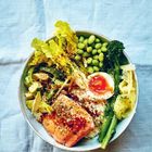 Eine Schüssel mit Lachs, Avocado, Ei, Brokkoli und Edamame auf hellem Stoffhintergrund.