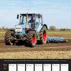 Ein blauer Traktor pflügt ein Feld mit einem Federzinkenegge. Kalender zeigt Februar 2027, Woche 8.