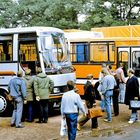 „Intercity bus“ ist auf einem grauen Bus zu lesen. Menschen stehen davor, teils mit Aktenkoffern. Bäume im Hintergrund.