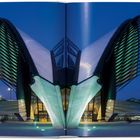 Keine Texte sichtbar. Modernes Gebäude bei Nacht mit futuristischem Design und blauer Beleuchtung, von einem Buch umrahmt.