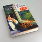 Auf einem Buchcover steht "DANIEL GLATTAUER", "IN EINEM ZUG". Illustration: Person am Zugfenster.