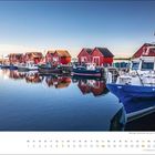 Februar Kalenderblatt: Rote Hütten und Boote spiegeln sich im Wasser, blauer Himmel im Hintergrund.