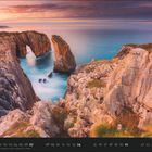 02. Kalenderdarstellung. Ansicht von Felsen mit Wasser und einem natürlichen Bogen. Sonnenuntergang sorgt für warmes Licht.