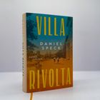 "VILLA RIVOLTA" von Daniel Speck. Roman Fischer. Zwei Personen laufen auf einem orangen Weg zwischen Bäumen.
