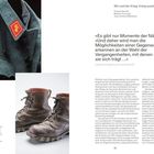 «Es gibt nur Momente der Nähe.» Graue Militärjacke mit rotem Abzeichen, Wanderstiefel, Text über Kriegsausstellungen.
