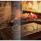 Schneeflocken links, Kaminfeuer rechts. In der Mitte ein Buch mit Brille darauf. Warme, gemütliche Atmosphäre.