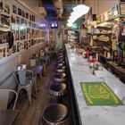 Poster mit "B&H MERCH!" und Produkten. Retro-Diner mit Marmortheke, runden Barhockern, Fotos an der Wand.