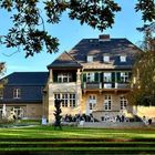 „Haus am Waldsee“; ein großes, elegantes Gebäude mit Garten, umgeben von Bäumen, Menschen sitzen vor der Fassade.