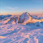 Verschneite Berglandschaft bei Sonnenaufgang, pinkes Licht auf den Gipfeln und dem Schnee.