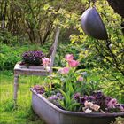 Ein alter Stuhl und eine Zinkwanne mit bunten Blumen in einem grünen, sonnenbeschienenen Garten.