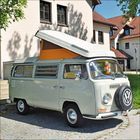 VW-Logo auf einem klassischen Campingbus mit aufgestelltem Dach vor einem Gebäude.
