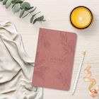 Auf einem hellen Holzuntergrund liegt ein rosa Notizbuch mit der Aufschrift "Zwoteausend24 sicher und wachst". Dazu Eukalyptus, eine Kerze und ein Bleistift.