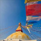 Bunte Gebetsfahnen wehen über einer buddhistischen Stupa, die sich gegen einen klaren blauen Himmel erhebt.