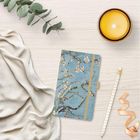 Notizbuch mit blühenden Zweigen, Kerze, Eukalyptus, Stoff, Bleistift und Geschenkband auf hellem Holz.