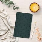 Kein Text im Bild. Ein Notizbuch mit dunkelgrünem Muster, Kerze, Zweig, Stoff und Bleistift auf hellem Tisch.