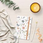 Keine sichtbaren Texte. Ein Notizbuch mit floralen Illustrationen, gelbe Kerze, Bleistift, Stoff und Eukalyptuszweig.