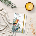 „Zweitausend dreiundzwanzig“ steht auf einem Notizbuch mit Papageien und Blättern. Daneben Kerze, Bleistift und Stoff.