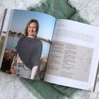 Text: "Lore Maxi". Eine Frau lächelt am Wasser in einem grauen Strickkleidungsstück. Daneben Beschreibungen und Anleitungen.