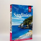 „Sardinien“, „Reise Know-How“. Illustration: Küste mit blauem Meer, klarem Himmel und Menschen am Strand.