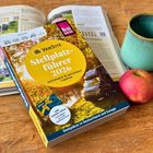 Cover: "VAN SITE Stellplatzführer 2026" auf einem Tisch mit Apfel, Tasse und offenem Buch im Hintergrund.