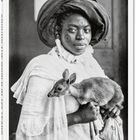 „Around the World in 125 Years“. Eine Frau mit Kopftuch hält behutsam ein kleines Reh.