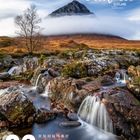 "Glen Coe, Scotland" in geschwungenen Buchstaben. Ein Baum, Berg mit Nebel, Wasserfall, Felsen und moosbedeckte Steine.