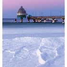 Seebrücke mit Tauchgondel in Zingst, Mecklenburg-Vorpommern. Winterlandschaft mit verschneiter Küste und violettem Himmel.