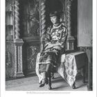 Anna May Wong: Eine Pionierin in Hollywood. Frau im traditionellen Kleid auf einem Tisch sitzend, umgeben von Kunstwerken.