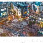 Eine geschäftige Kreuzung mit vielen Menschen, umgeben von Gebäuden mit großen Leuchtreklamen und bunten Werbetafeln.