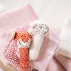 Zwei gehäkelte Baby-Spielzeuge, Fuchs und Schaf, liegen auf rosa Stoffen.