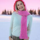 Kein sichtbarer Text. Eine lächelnde Person in Winterkleidung vor einem rosa Himmel. Trägt eine pinke Mütze und Schal.