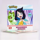 "Pokémon", "WILLKOMMEN IN PALDEA", "NELSON". Illustration: Mädchen mit Pokémon und Blatt in der Hand, bunte Hintergrundstrahlen.