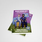 Buchtitel: „DAS DING IST“. Zwei Personen auf einem Stuhl vor lila Hintergrund und Blumenmuster.