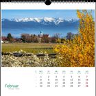 Kalenderseite Februar mit schneebedeckten Bergen, blühendem Baum und Kirche im Hintergrund.