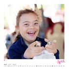 Kalenderblatt April. Ein lachendes Kind mit lockigem Haar drückt etwas mit den Händen.