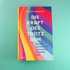Text: "DIE KRAFT DES TROTZ DEM: WIE MAN WEITERMACHT, AUCH WENN'S SCHWIERIG WIRD." Buntes Buchcover mit geschwungenen Linien.